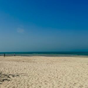 A quiet, untouched stretch of Al Jurf Hidden Beach with golden sand, turquoise waters, and a clear blue sky.