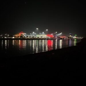 A vibrant night scene at Al Zeina Beach, with colorful city lights reflecting on the calm waterfront, highlighting the marina and modern architecture.