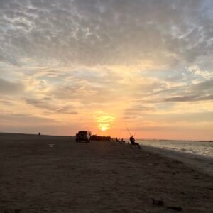 A peaceful sunset on the Hidden Hameem Beach in Abu Dhabi, with a couple of fishing rods planted on the ground and a car parked nearby, creating a peaceful and colorful beach retreat.