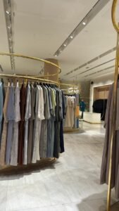 Elegant abaya boutique in Abu Dhabi displaying modern modest fashion with pastel and neutral abayas on gold racks. 
