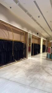 Inside Mauzan Abu Dhabi boutique showing neatly arranged abaya fabrics and black modest abayas on gold racks