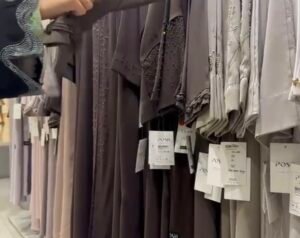 Assorted abayas hanging in Posh Abaya store Abu Dhabi, showing neutral tones and embellished fabric details.