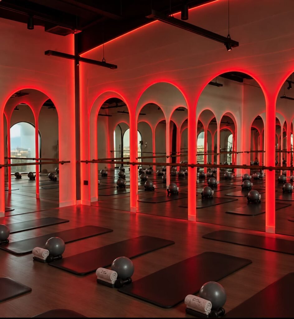 Interior of BRRN Barre's heated fitness studio in Abu Dhabi, featuring red lighting, mirrors, and barre workout equipment.