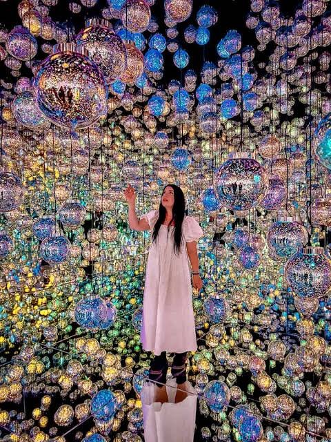 A woman exploring indoor activities and immersive art installation filled with colorful, glowing and mirrored reflections.